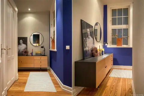 Flur mit Wand in tiefem Indigo, Holzmöbel, Spiegel und Kunstwerk. Ein Streifenmuster auf dem Teppich ergänzt die Szene.