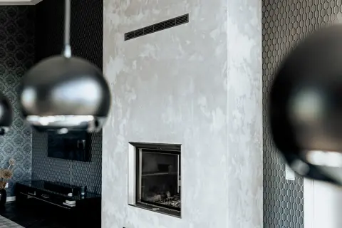 Edler Kamin mit Wischtechnik Wand in Grau. Daneben eine Wand mit geometrischem Muster und ein Teil einer Hängeleuchte.