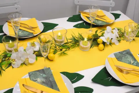 Sommerliche tischdeko mit zitronen, Orchideen und Kerzen. Gelbe Servietten und goldene Besteckteile runden das Bild ab.