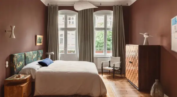Ein Schlafzimmer in warmen, gedeckten Farben. Braune Wände, ein gemustertes Kopfteil und ein helles Bett schaffen eine gemütliche Atmosphäre.