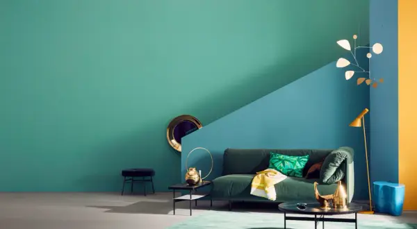 Ein Wohnzimmer mit petrolfarbener Wand, die zu einem blauen und gelben Bereich übergeht. Welche Farbe passt zu Petrol? Hier: Grün, Gold und Blau.