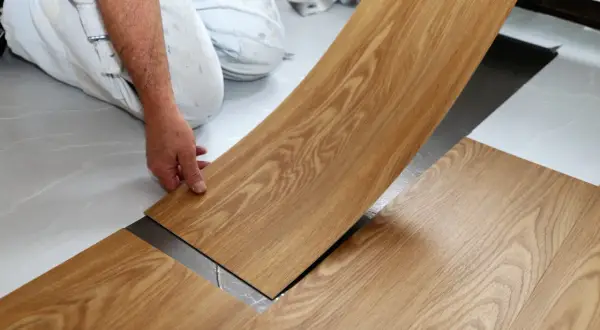 Hand verlegt Holzoptik-Vinylboden. Die Dielen werden präzise nebeneinander gelegt, um ein schönes Ergebnis zu erzielen.