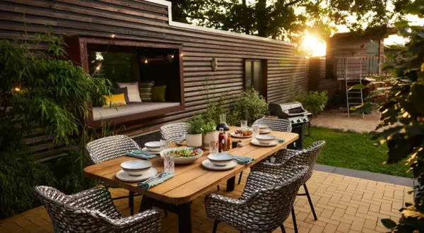 Eine schmale Terrasse gestalten: Gemütlicher Essbereich mit Holztisch, Rattanstühlen, Grill und Sitznische mit Kissen.