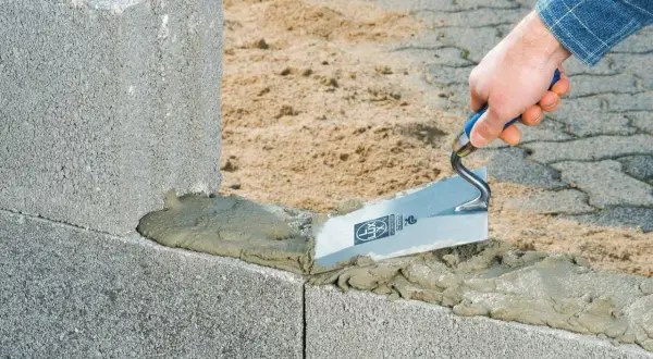Maurer trägt Mörtel mit Kelle auf Betonsteine auf. Der Unterschied zwischen Beton und Zement wird hier beim Bau deutlich.