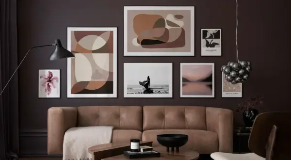 Ein braunes Ledersofa vor einer Wand mit abstrakter Kunst und einem Foto. Welche Farbe passt zu Schwarz? Hier: Braun und Beige.