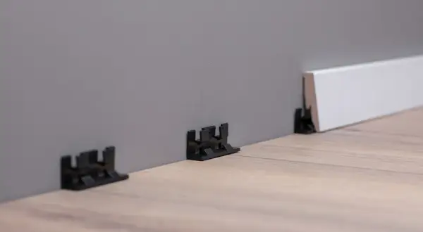 Schwarze Clips zur einfachen Montage von Sockelleisten an der Wand.