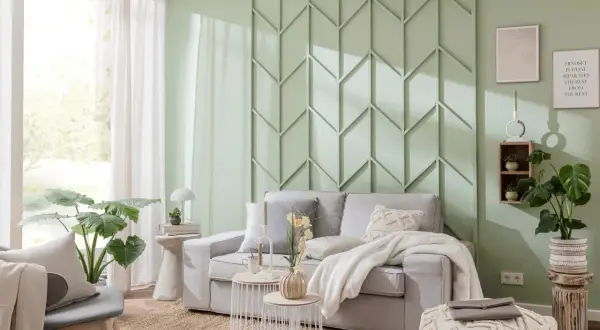 Moderne Wandgestaltung im Wohnzimmer hinter der Couch mit geometrischen Mustern in Mintgrün. Gemütliche Couch mit Kissen und Decke.