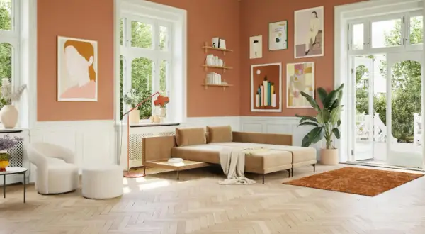 Ein gemütliches Wohnzimmer mit orangefarbenen Wänden. Ein beiger Teppich und ein Sofa, welche farbe passt zu orange, harmonieren perfekt.