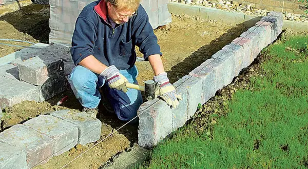 Mann setzt mit Hammer und Richtschnur präzise Rasenkantensteine, um den Garten zu gestalten.
