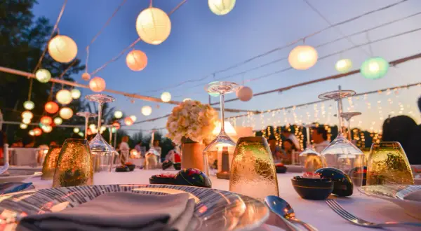 Festlich gedeckte Tafel mit bunten Lampions als Dekoideen Hochzeit im Garten. Gläser, Blumen und Lichterketten schaffen romantische Stimmung.