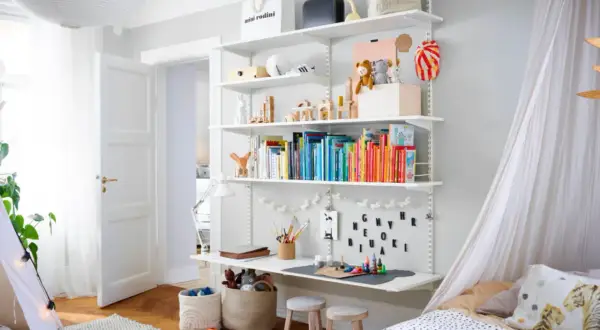 Ein schmal eingerichtetes Kinderzimmer mit einem Regal voller Bücher und Spielzeug, einem Schreibtisch und einem Bett mit Baldachin.