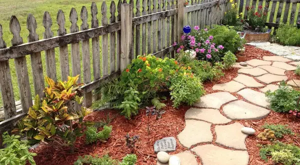 Natürliche Steinplatten formen einen geschwungenen Gartenweg, umgeben von bunten Blumen und grünen Pflanzen. Tolle Gartenweg Ideen für Ihr Zuhause.