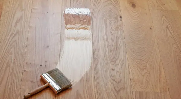 Breite Pinsel trägt Lack auf einen hellen Holzdielenboden auf. Der Prozess, einen Dielenboden zu versiegeln, beginnt.