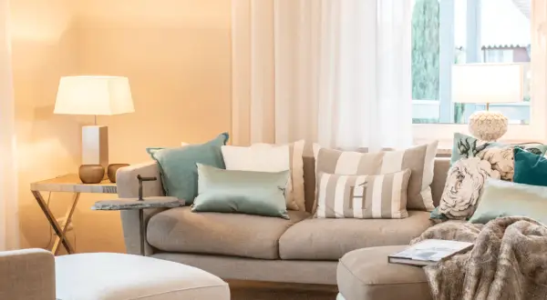 Ein beiges Sofa mit vielen Kissen, darunter gestreifte und florale Muster, lädt zum Entspannen ein.