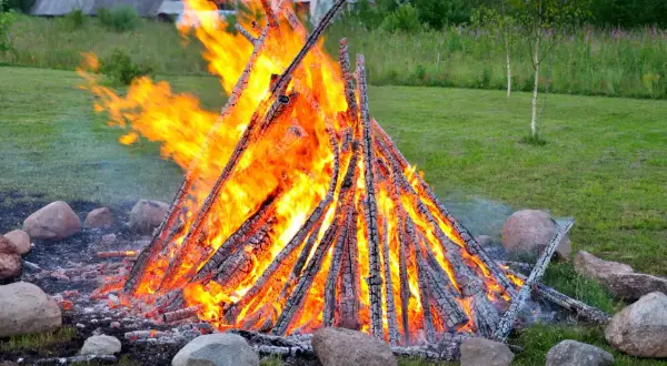 Ein großes, loderndes lagerfeuer im garten, umgeben von Steinen. Die Flammen tanzen hoch und erhellen die grüne Wiese.