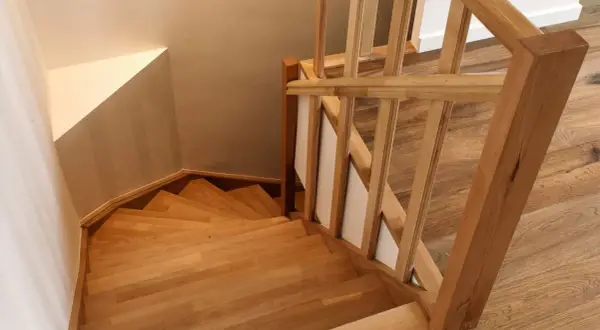 Holztreppe mit geschwungenen Treppenstufen. Der Handlauf und die Stufen sind aus hellem Holz gefertigt, was den Eindruck von Wärme und Natürlichkeit vermittelt. Die Treppenstufen streichen ist hier nicht nötig, da das Holz bereits schön zur Geltung kommt.