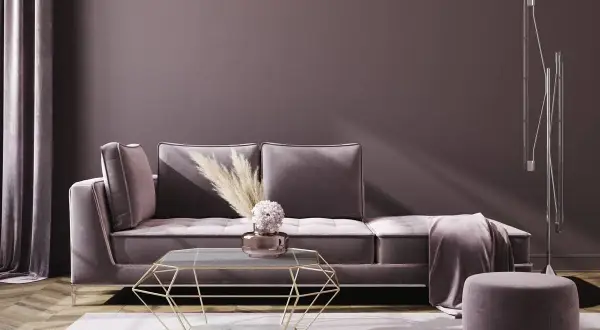 Ein gemütliches Wohnzimmer in mauve Farbe mit einem Samtsofa, einem geometrischen Couchtisch und einem Hocker.