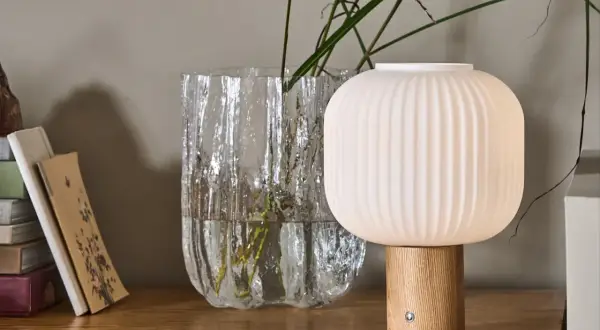 Eine skandinavische tischlampe holz mit geripptem Schirm und Holzfuß steht neben einem Glasvase mit Gräsern.