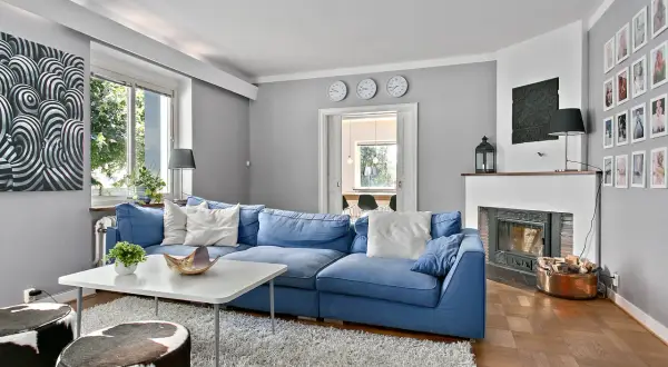 Blau und Weiß passen wunderbar zu Grau. Ein gemütliches Wohnzimmer mit blauem Sofa, weißem Teppich und Kunst an der Wand.