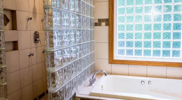 Badezimmer mit Dusche und Badewanne, umgeben von Glasbausteinen. Die Glasbausteine verlegen schafft ein helles und modernes Ambiente.