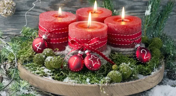 Ein **ausgefallener Adventskranz** mit vier roten Kerzen, geschmückt mit Moos, Tannenzweigen und kleinen Kugeln mit den Zahlen 1, 2, 4.