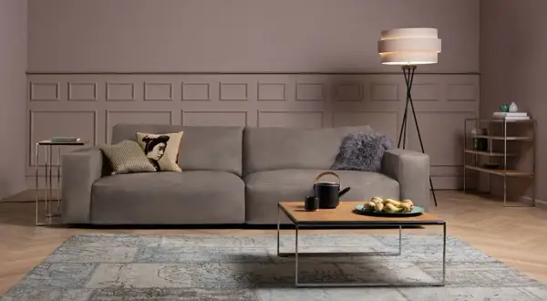 Ein taupefarbenes Sofa mit Kissen und ein Couchtisch mit Obstschale. Welche Farbe passt zu Taupe? Hier sehen Sie eine elegante Kombination mit Blau und Grau.