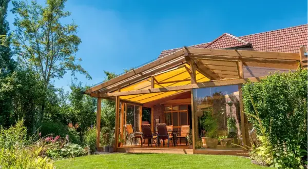 Ein moderner Wintergartenanbau mit Glasfront und gelbem Sonnensegel bietet tolle anbau wintergarten ideen. Gemütliche Sitzmöbel laden zum Verweilen ein.
