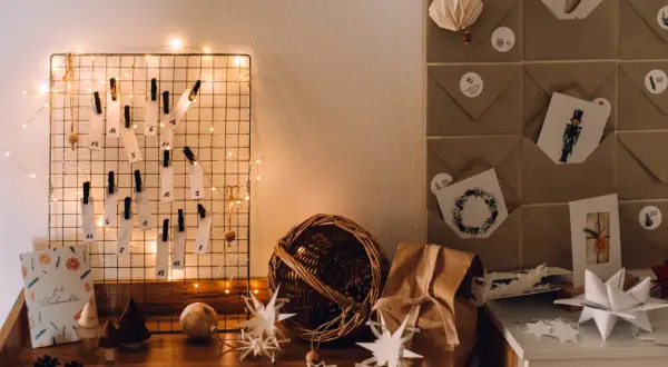 DIY Adventskalender Ideen: Ein Drahtgitter mit nummerierten Zetteln und Lichterkette, daneben braune Briefumschläge mit Weihnachtsmotiven.