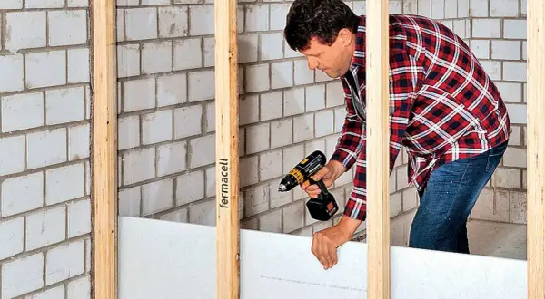 Mann baut eine Trennwand mit Gipskartonplatten und Akkuschrauber.