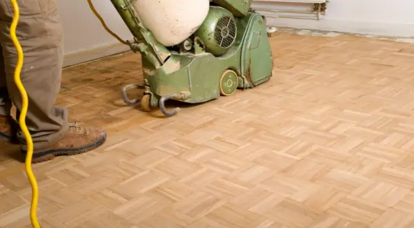 Mann schleift Parkett mit einer Maschine. Der Boden wird für eine neue Oberflächenbehandlung vorbereitet.
