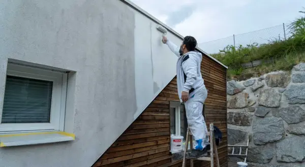 Mann streicht mit Rolle eine Hausfassade. So streicht man eine Fassade: Schritt für Schritt zum neuen Look.