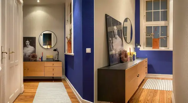 Flur mit Wand in tiefem Indigo, Holzmöbel, Spiegel und Kunstwerk. Ein Streifenmuster auf dem Teppich ergänzt die Szene.