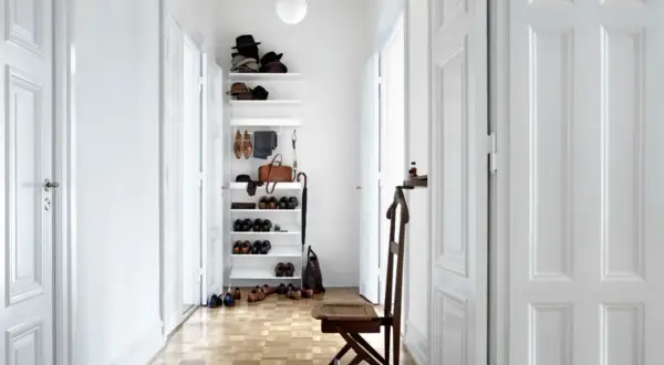 Helle Türen und ein weißes Regal lassen den schmalen Flur optisch breiter wirken. Schuhe und Hüte sind ordentlich verstaut.