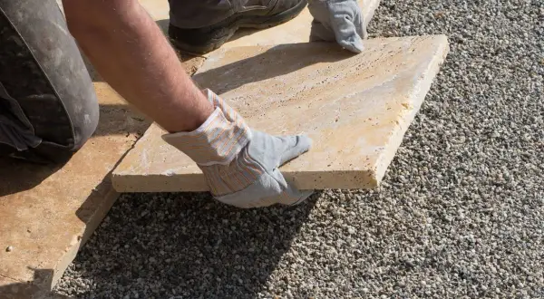 Arbeiter verlegt sorgfältig eine helle Terrassenplatte auf Kies.