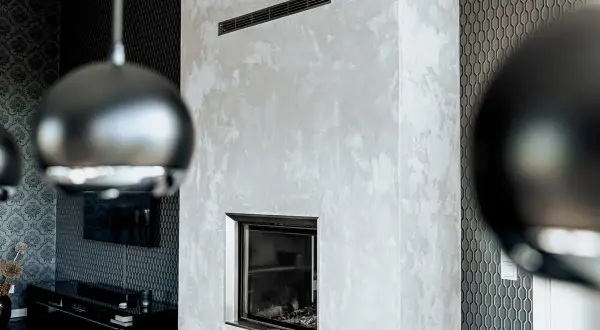 Edler Kamin mit Wischtechnik Wand in Grau. Daneben eine Wand mit geometrischem Muster und ein Teil einer Hängeleuchte.