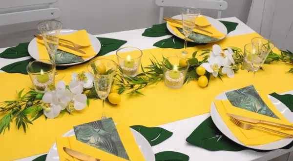 Sommerliche tischdeko mit zitronen, Orchideen und Kerzen. Gelbe Servietten und goldene Besteckteile runden das Bild ab.