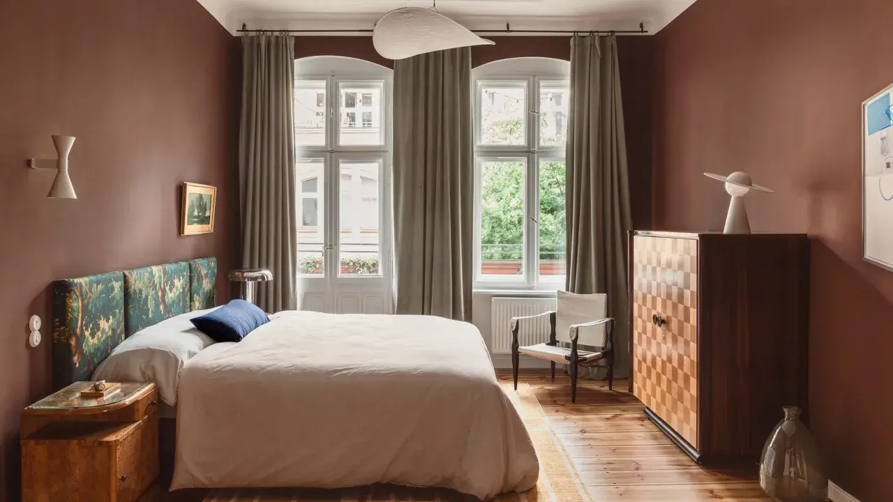 Ein Schlafzimmer in warmen, gedeckten Farben. Braune Wände, ein gemustertes Kopfteil und ein helles Bett schaffen eine gemütliche Atmosphäre.