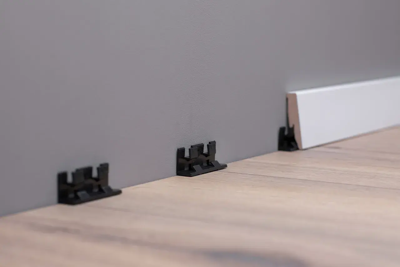 Schwarze Clips zur einfachen Montage von Sockelleisten an der Wand.