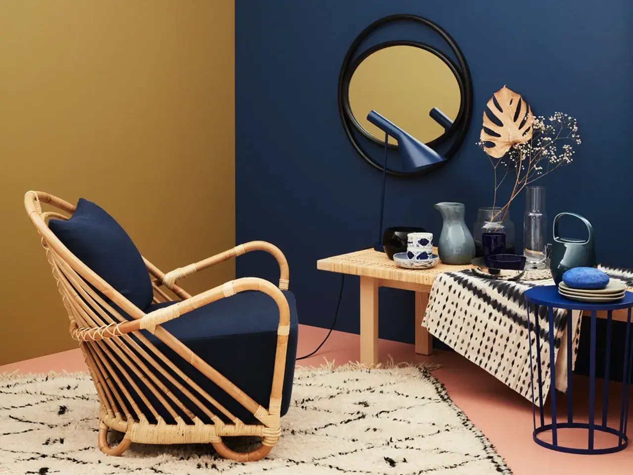 Ein Rattansessel mit dunkelblauem Kissen steht auf einem Teppich. Welche Farbe passt zu Gold? Hier: ein goldener Spiegel und eine gelbliche Wand.