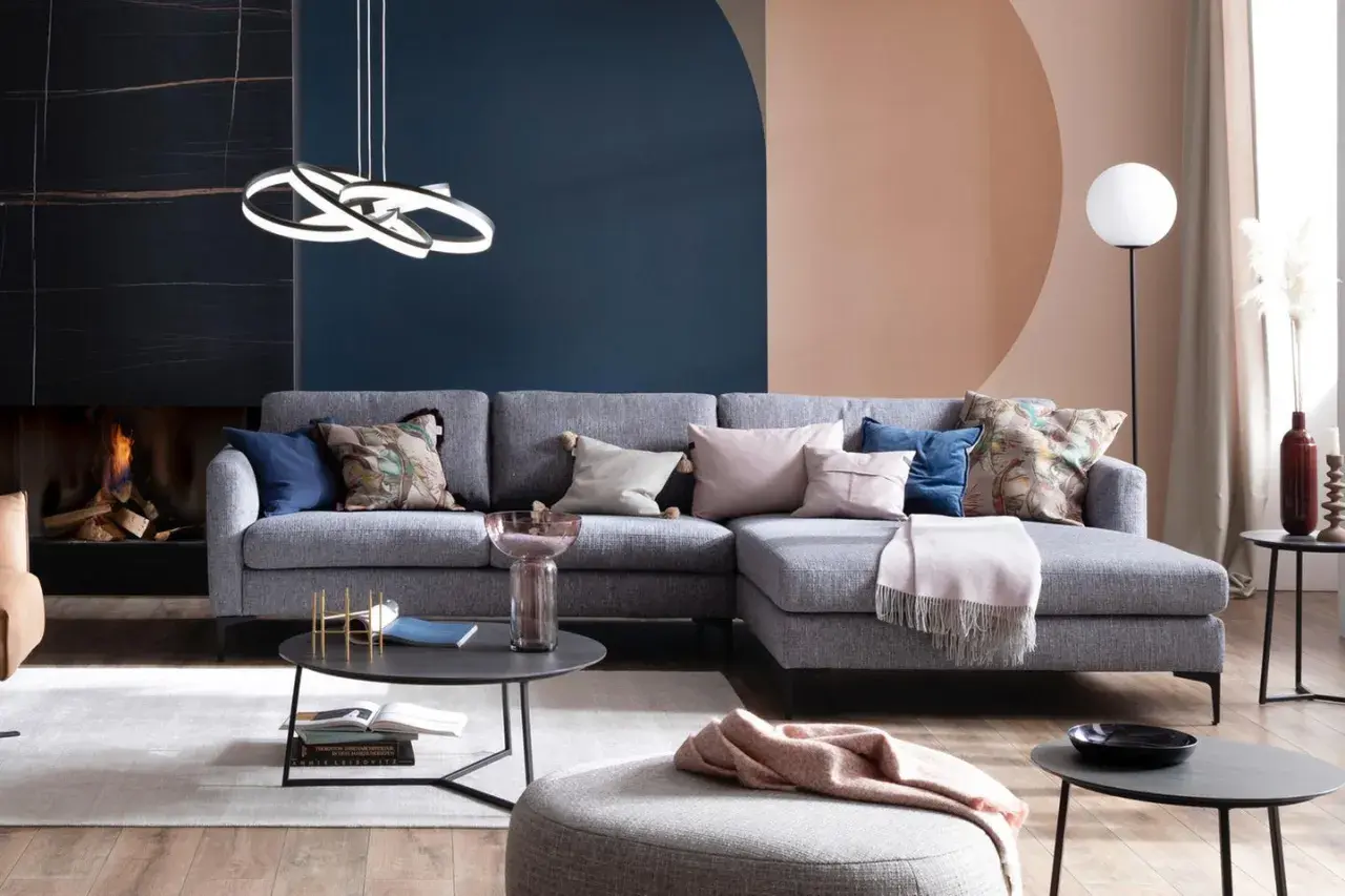 Stilvolle Ideen für ein graues Sofa: Kissen in Rosa, Blau und mit Blattmuster, eine Decke und ein Beistelltisch schaffen Gemütlichkeit.