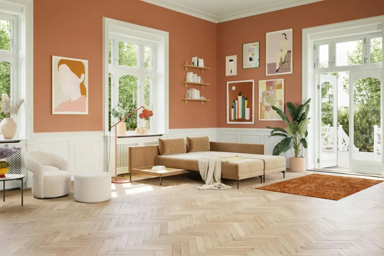 Ein gemütliches Wohnzimmer mit orangefarbenen Wänden. Ein beiger Teppich und ein Sofa, welche farbe passt zu orange, harmonieren perfekt.