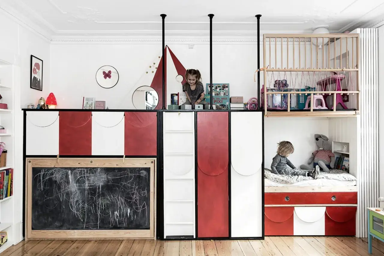 Kreative geschwisterzimmer ideen: Kinder spielen in einem bunten Zimmer mit Hochbetten, Rutsche und Tafel.