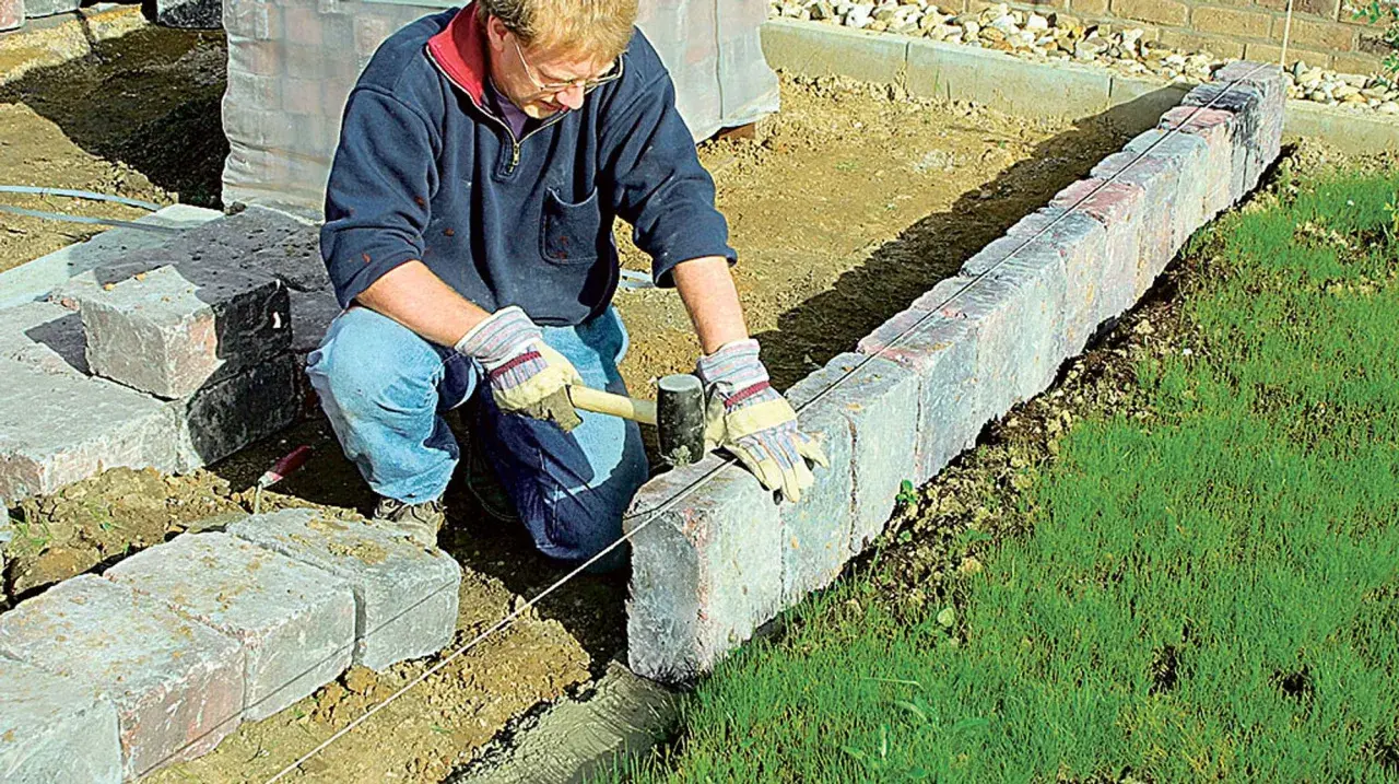 Mann setzt mit Hammer und Richtschnur präzise Rasenkantensteine, um den Garten zu gestalten.