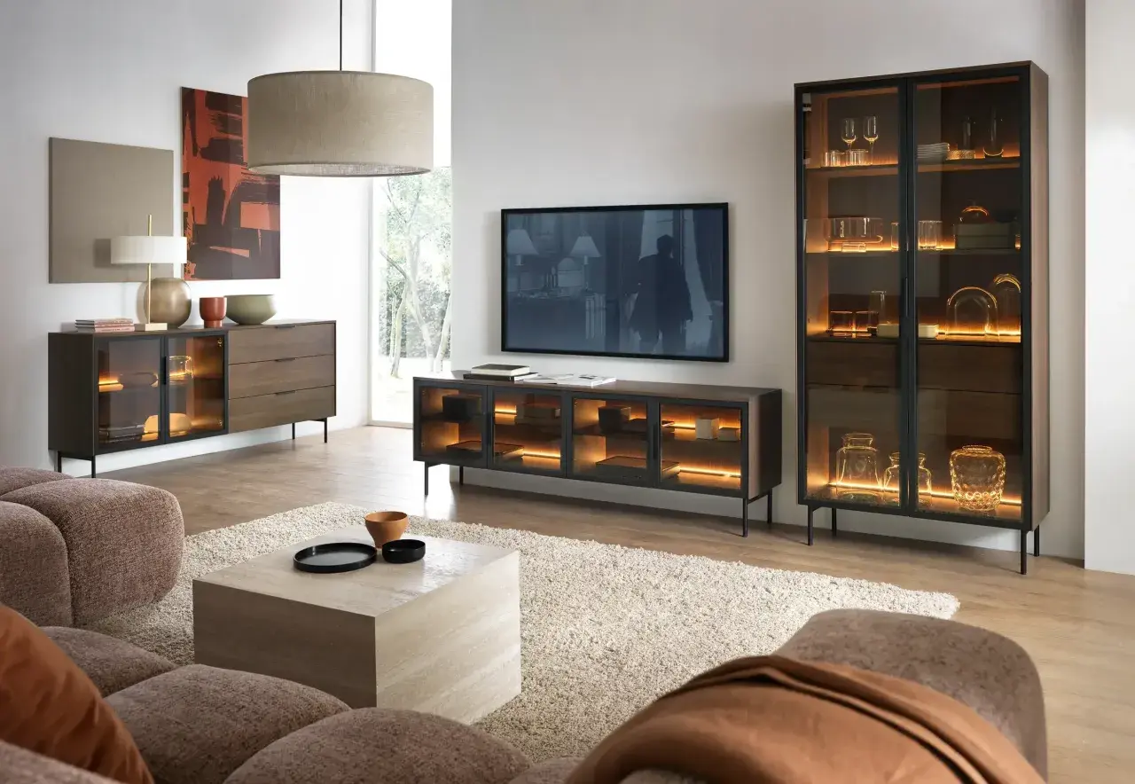 Ein stilvolles Wohnzimmer, in dem sich grau und braun harmonisch ergänzen. Ein beiger Teppich und eine braune Couch bilden die Basis, während dunkle Holzmöbel mit integrierter Beleuchtung Akzente setzen.
