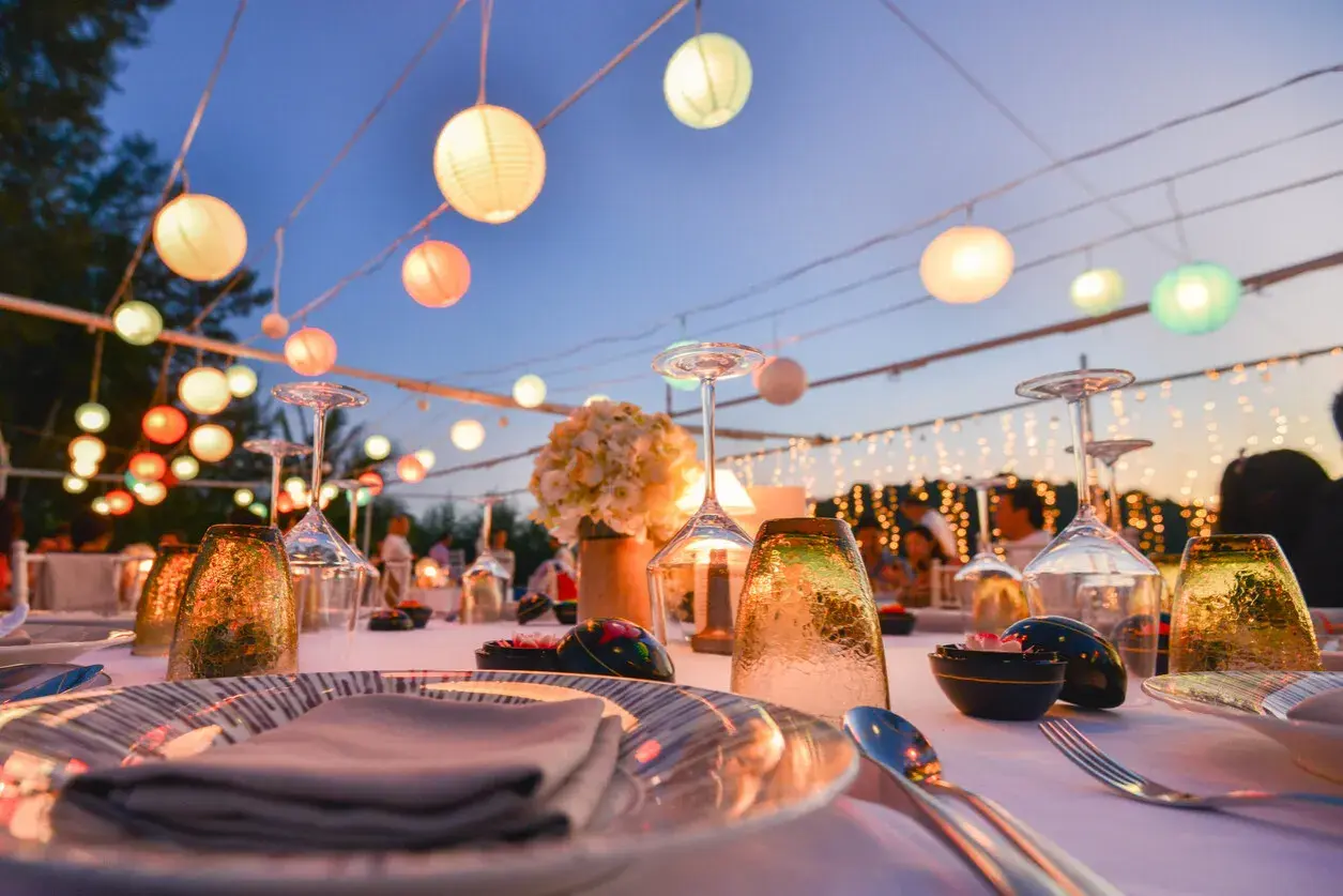 Festlich gedeckte Tafel mit bunten Lampions als Dekoideen Hochzeit im Garten. Gläser, Blumen und Lichterketten schaffen romantische Stimmung.