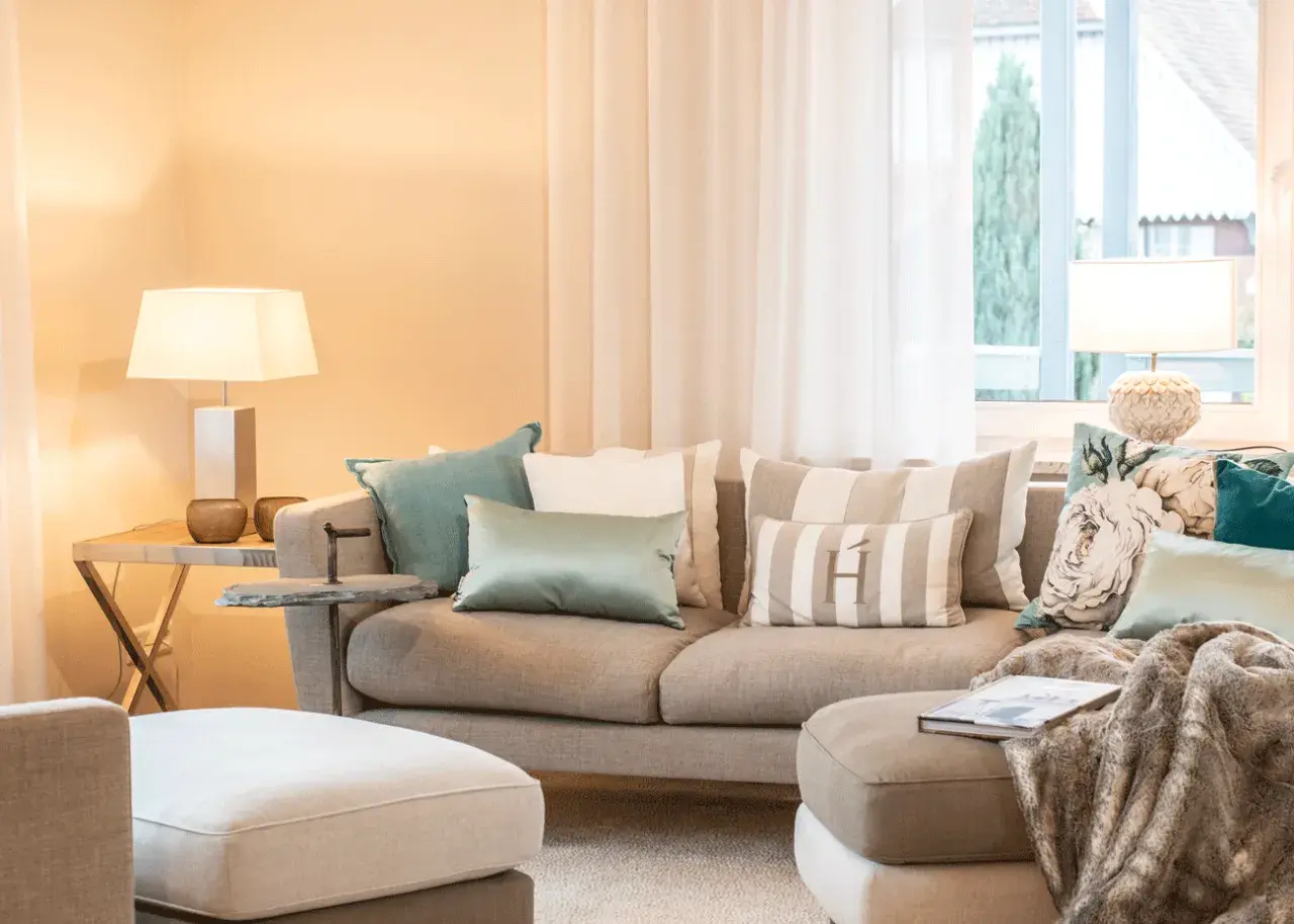 Ein beiges Sofa mit vielen Kissen, darunter gestreifte und florale Muster, lädt zum Entspannen ein.
