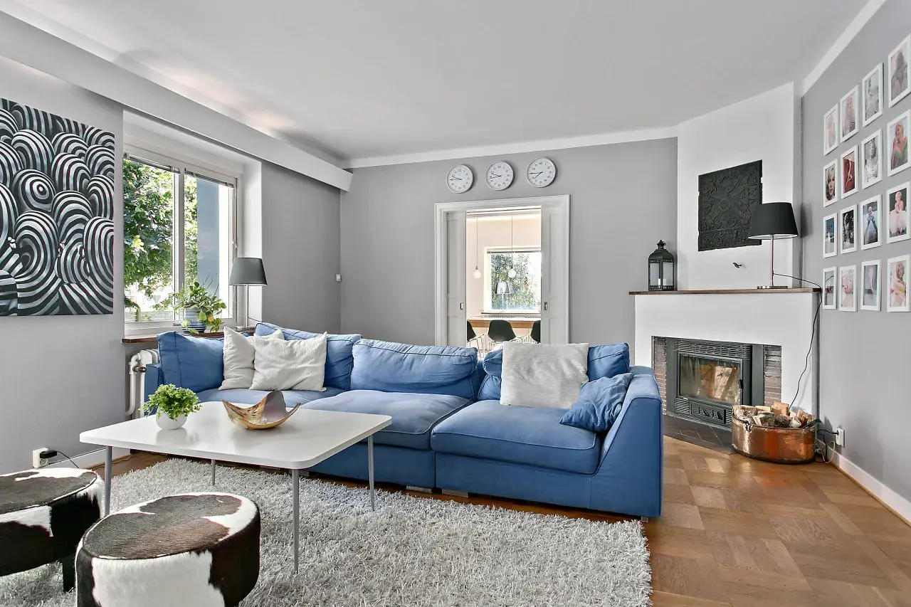 Blau und Weiß passen wunderbar zu Grau. Ein gemütliches Wohnzimmer mit blauem Sofa, weißem Teppich und Kunst an der Wand.