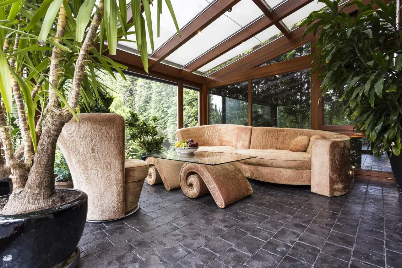 Gemütliches Ambiente im Wintergarten: Einladende Couch, geschwungener Glastisch und üppige Pflanzen laden zum Entspannen ein. Perfekt, um den Wintergarten einzurichten.