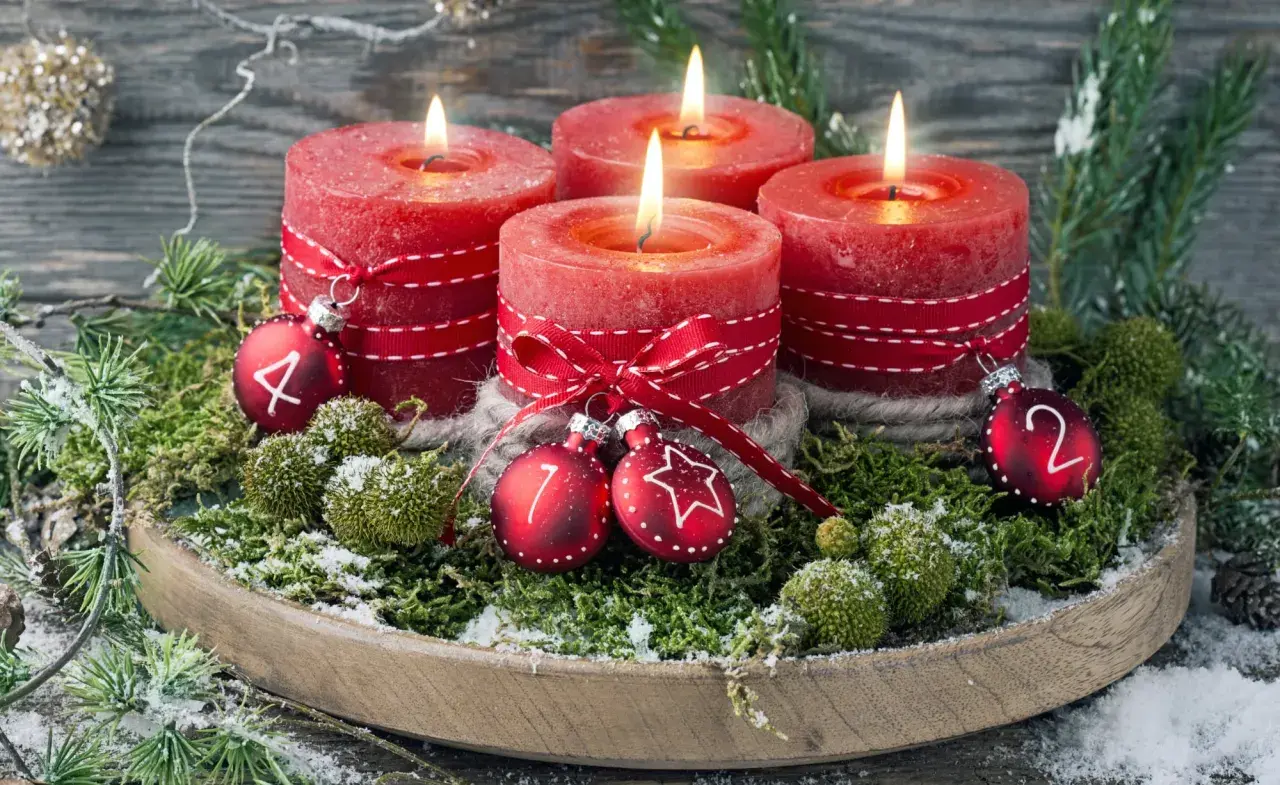 Ein **ausgefallener Adventskranz** mit vier roten Kerzen, geschmückt mit Moos, Tannenzweigen und kleinen Kugeln mit den Zahlen 1, 2, 4.