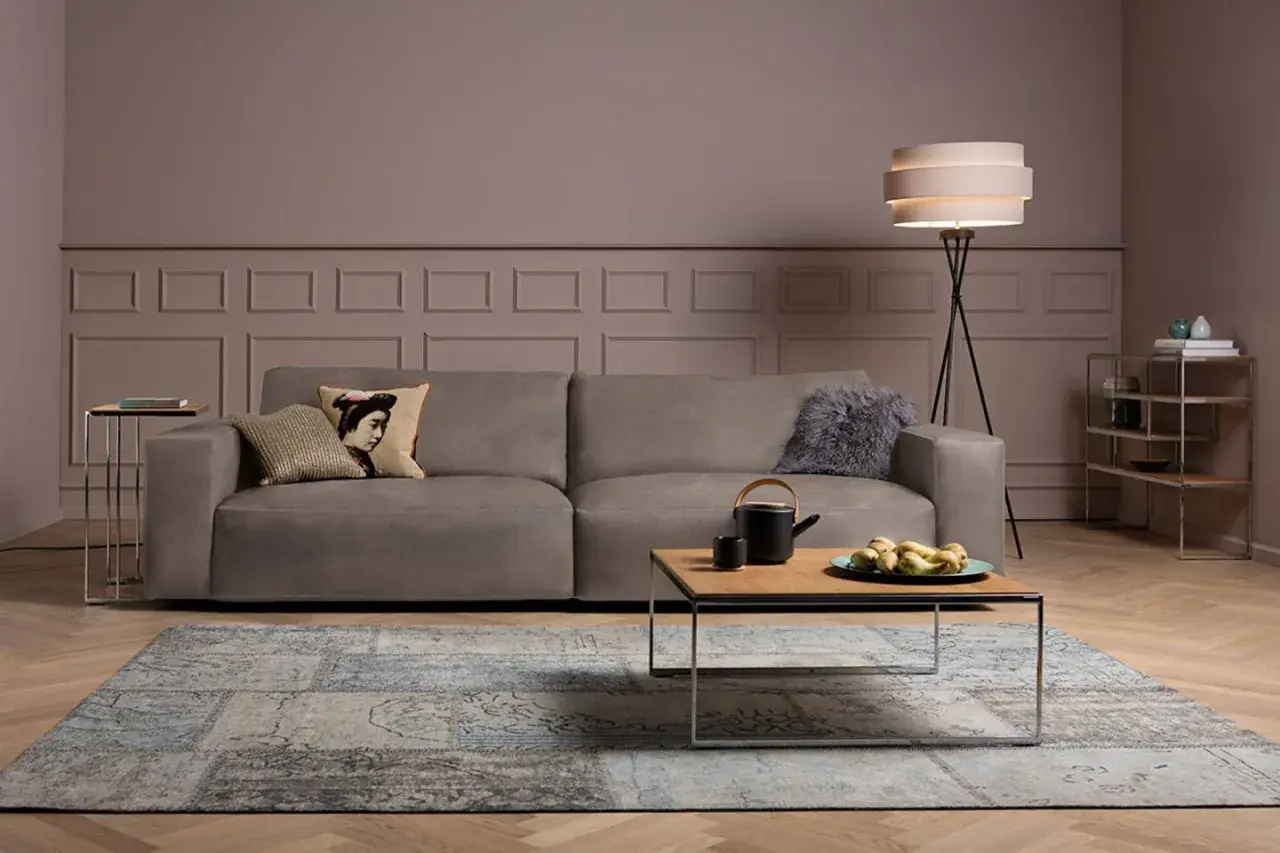 Ein taupefarbenes Sofa mit Kissen und ein Couchtisch mit Obstschale. Welche Farbe passt zu Taupe? Hier sehen Sie eine elegante Kombination mit Blau und Grau.
